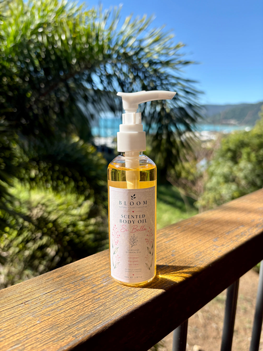 Si Bella scented body oil 100 mL with white pump on a timber railing overlooking Airlie Beach