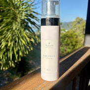 Bloom Organics Balance Cleanser, 200 mL pump bottle on a wooden railing with greenery behind it.
