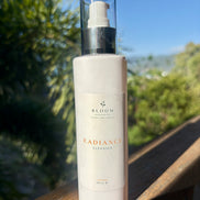 Bloom Organics Radiance Cleanser, 200 mL pump bottle on a wooden railing with greenery behind it.