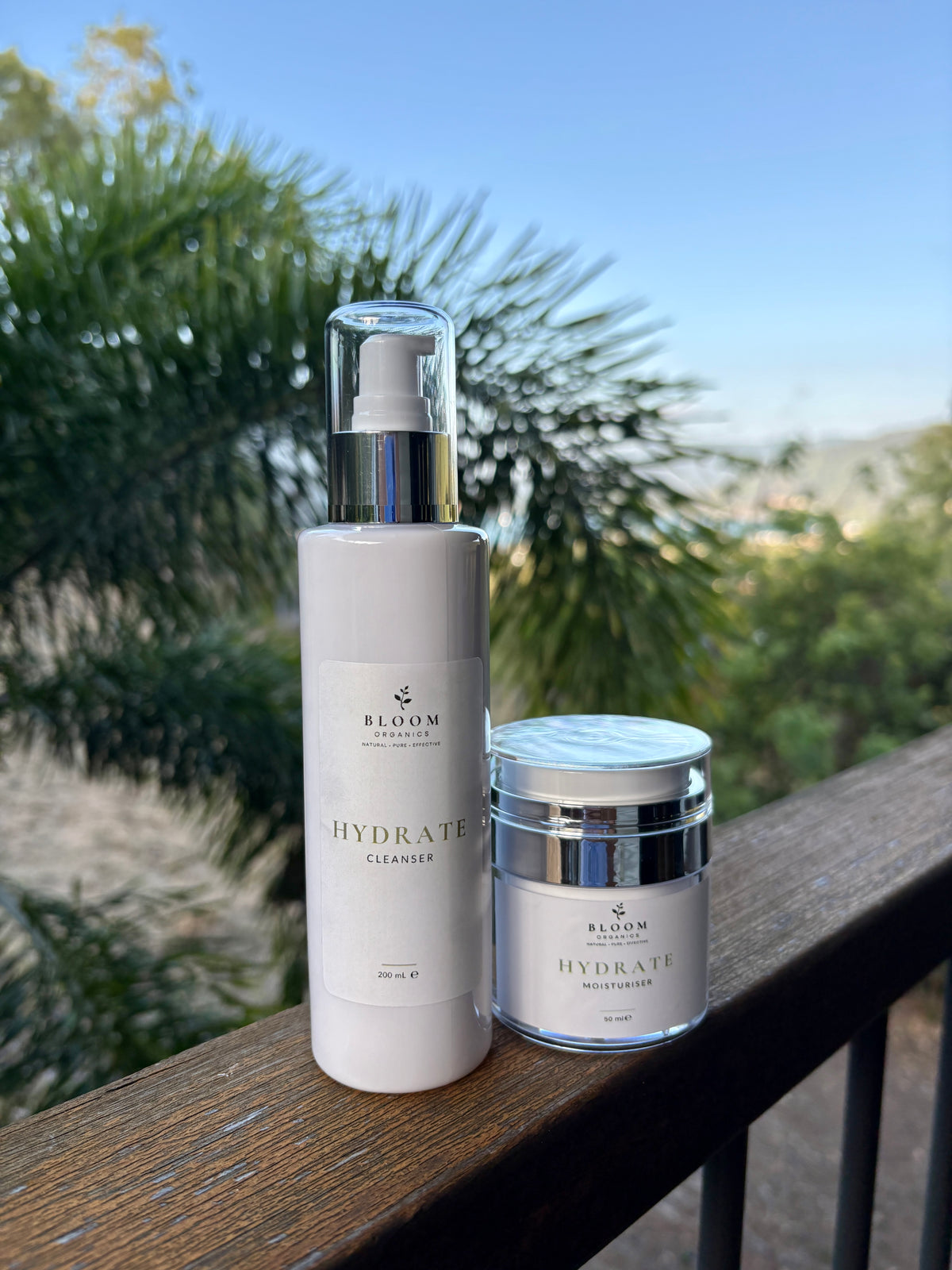 Hydrate Cleanser and Moisturiser on a timber railing with tropical foliage